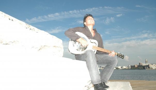 man sitting on white step playing white guitar