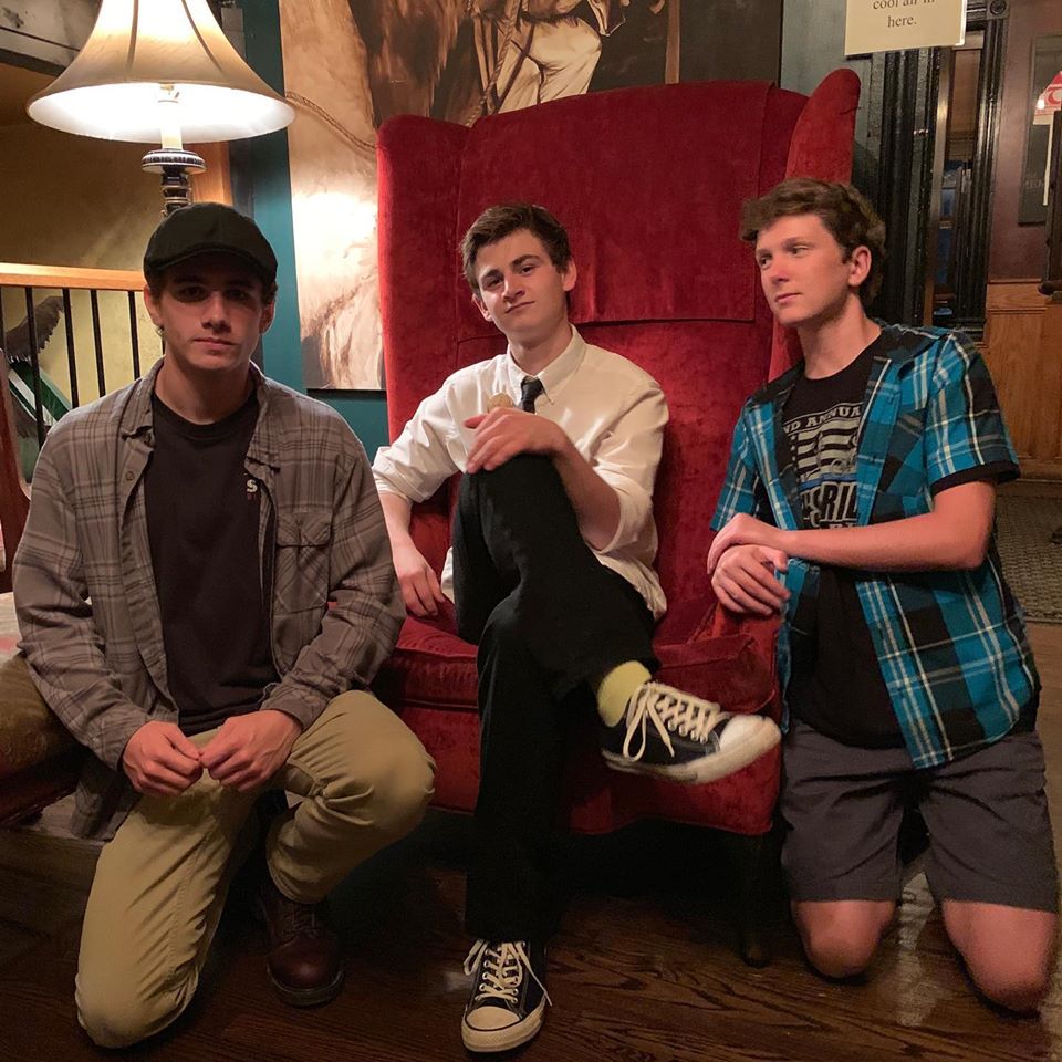 3 young men posing with red chair